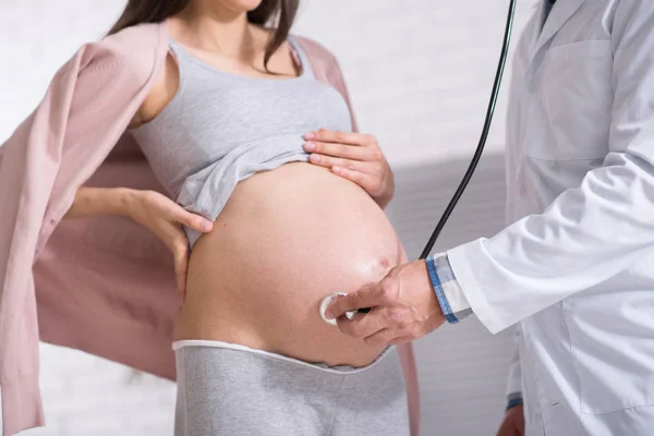 Médico competente poniendo parte del estetoscopio en el vientre del bebé —  Fotos de Stock