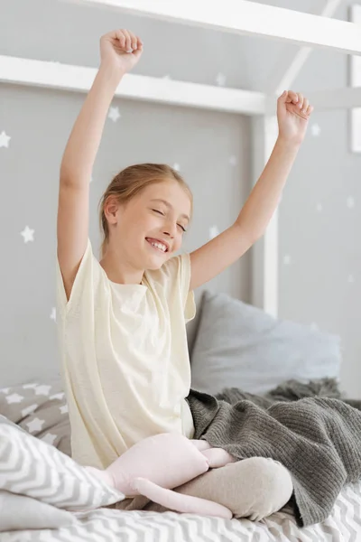Excited child sitting on bed with hands in air — Stock Photo, Image