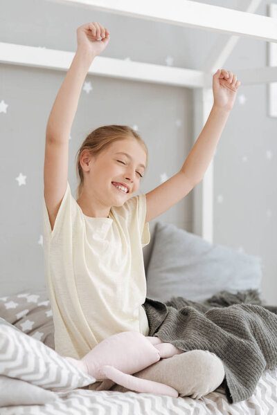 Excited child sitting on bed with hands in air