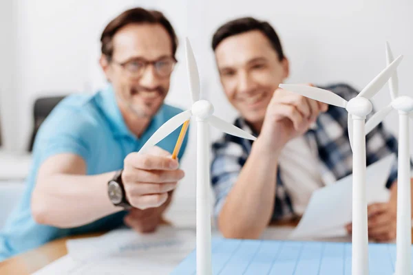 Gülümseyen adam bir rüzgar türbini modeline kalemle işaret — Stok fotoğraf