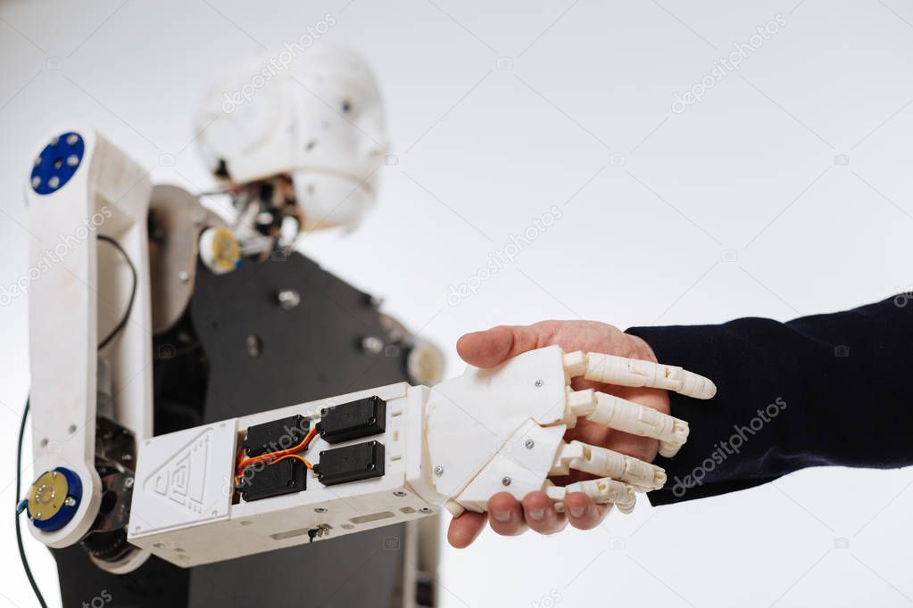 White elaborate robot shaking hands with human