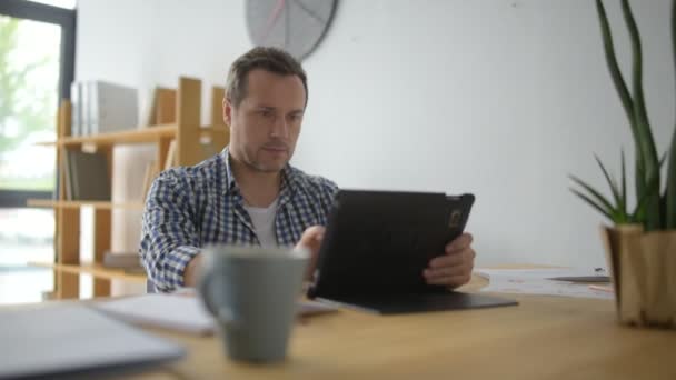 Konzentrierter erwachsener Mann sitzt am Tisch — Stockvideo