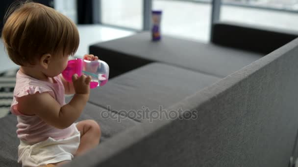 Милый малыш пьет воду на диване. — стоковое видео