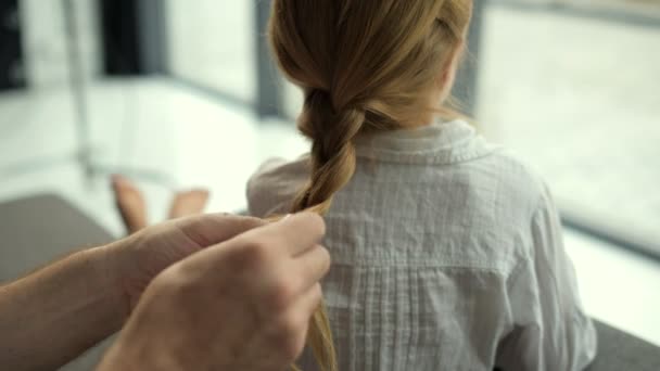 Заботливый отец, сплетающий волосы дочери дома — стоковое видео