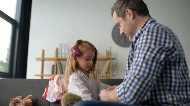 Люблячий батько регулює ролики для волосся на волоссі своєї красивої маленької дочки — стокове відео