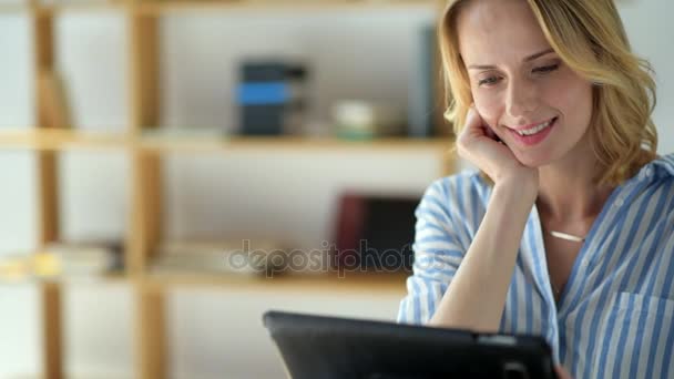 Strålande kvinna tittar på en tablett dator medan de studerar hemma — Stockvideo