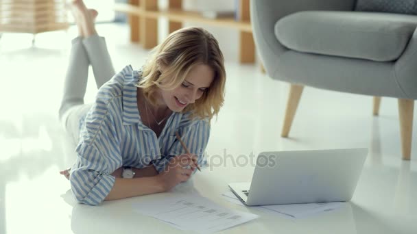 Freelancer feminino pensativo trabalhando com documentos enquanto deitado no chão — Vídeo de Stock