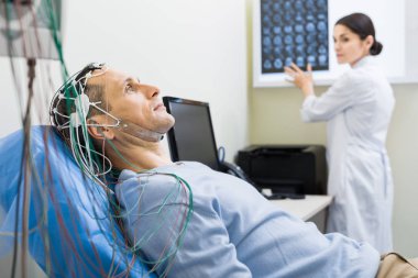 Female doctor carrying out electroencephalography of man clipart