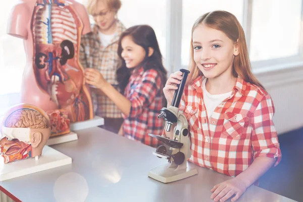 Позитивная восторженная девушка стоит рядом с микроскопом — стоковое фото