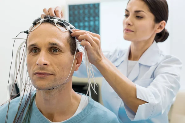 Женщина-врач фиксирует электроды на голове пациента — стоковое фото