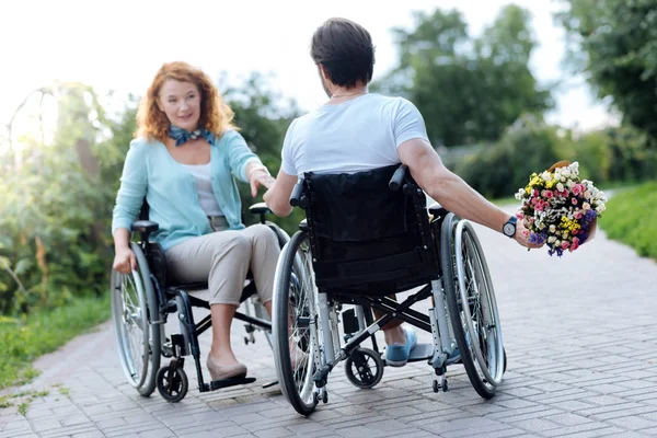 Ευχάριστη wheelchaired άνθρωπος παρουσιάζοντας λουλούδια συζύγου — Φωτογραφία Αρχείου