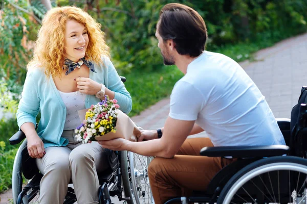 Mujer alegre en silla de ruedas recibiendo un ramo de flores — Foto de Stock