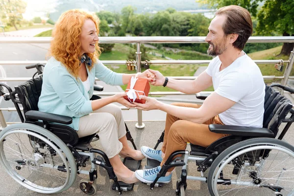 Pareja con silla de ruedas positiva sosteniendo un regalo — Foto de Stock