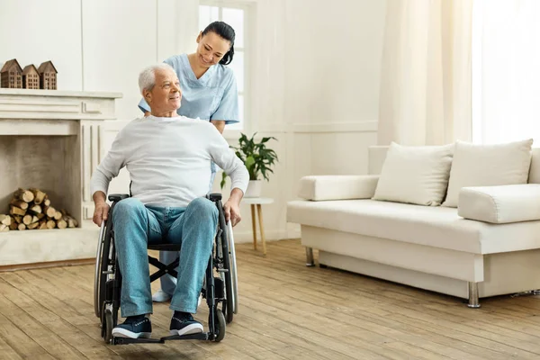 Allegro caregiver positivo spostare una sedia a rotelle — Foto Stock