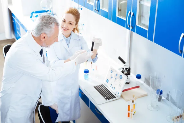 Assistente de laboratório positivo mostrando reagente preto para seu colega — Fotografia de Stock
