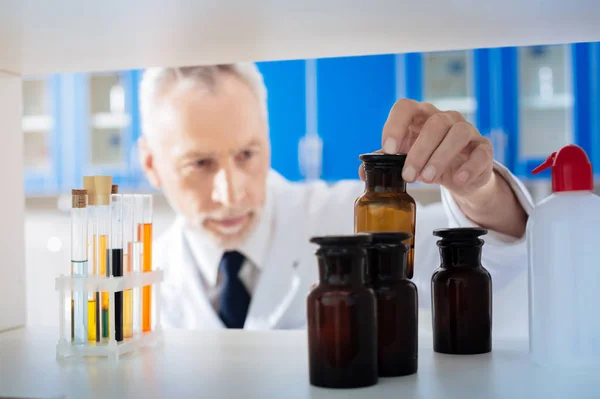 Serious man raising necessary bottle — Stock Photo, Image