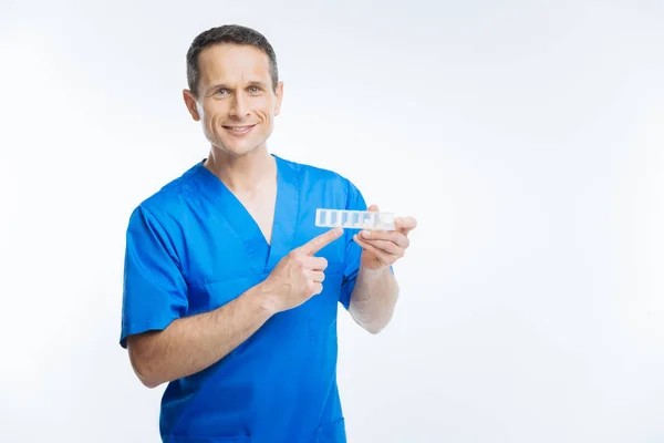 Дружелюбный врач указывает на органайзер таблеток — стоковое фото