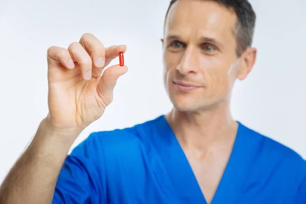 Positive minded doctor looking at red pill — Stock Photo, Image