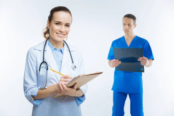 Cheerful doctor with notebook smiling into camera — Stock Photo, Image