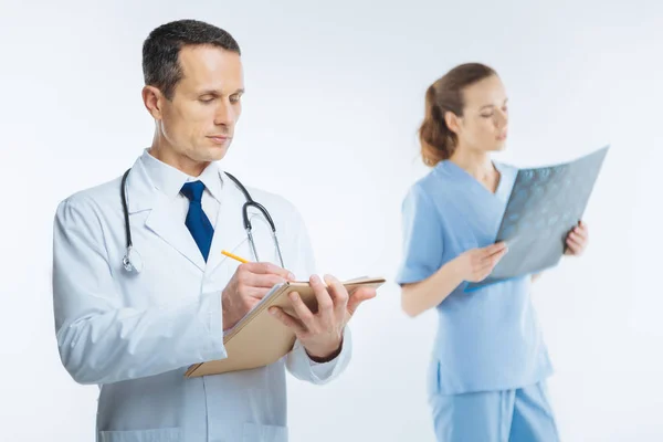 Confident doctor with stethoscope making notes — Stock Photo, Image
