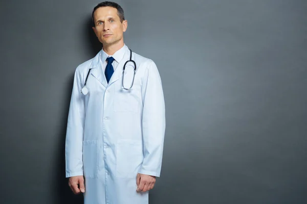 Médico masculino sério posando para câmera sobre fundo cinza — Fotografia de Stock