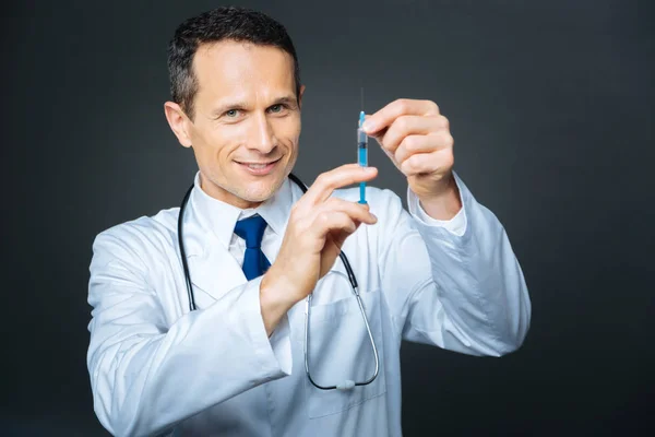 Médico sonriente posando con jeringa sobre fondo — Foto de Stock