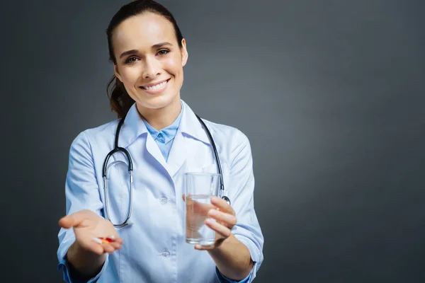 Jeune femme réfléchie en manteau blanc tenant pilules et eau — Photo