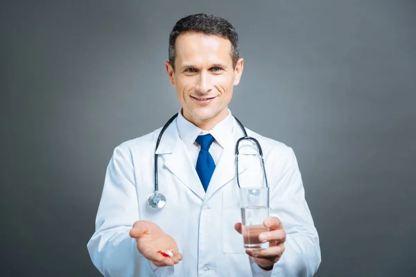Thoughtful mature man in white coat holding pills and water — Stock Photo, Image