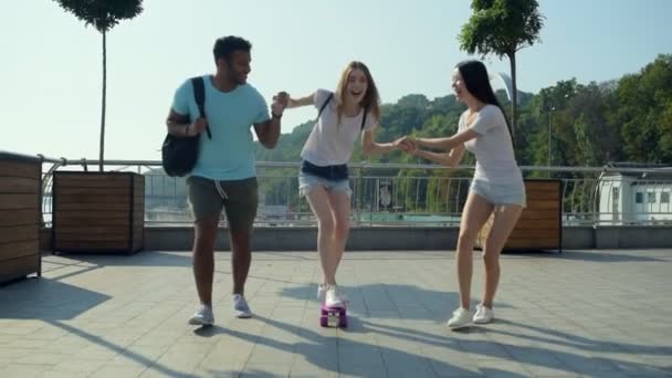 Позитивная девушка учится кататься на скейтборде с друзьями — стоковое видео