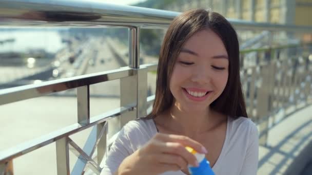 Atrakcyjny azjatycki dziewczyna dmuchanie bańki, stojąc na moście — Wideo stockowe
