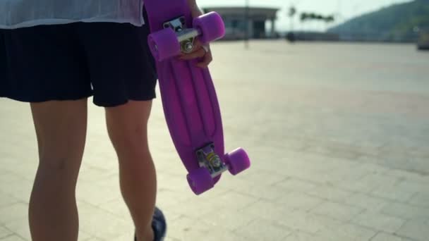 Вид ззаду гарненька дівчина зі скейтбордом, що виходить на вулицю — стокове відео