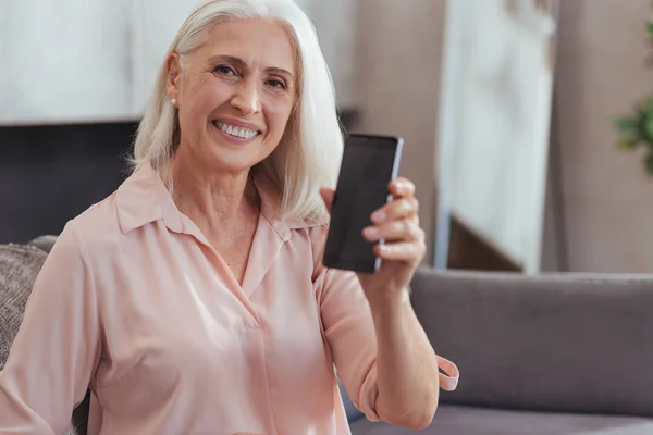 Cintura para cima de uma mulher idosa alegre mostrando seu novo smartphone — Fotografia de Stock