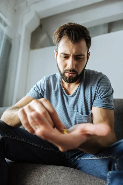 Homem barbudo infeliz olhando para a palma da mão com pílulas — Fotografia de Stock