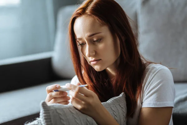 Mujer joven triste mirando el termómetro — Foto de Stock