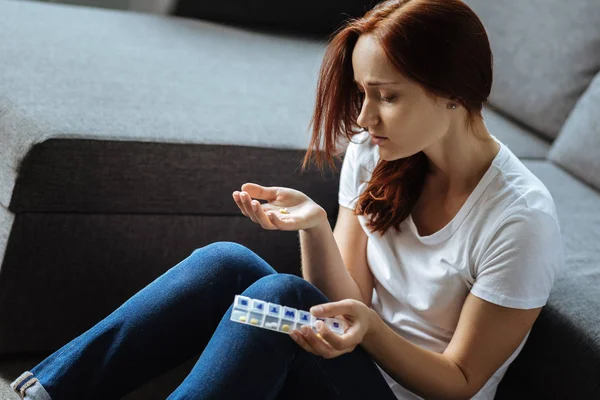 忧郁的年轻女子，看着她的药丸 — 图库照片