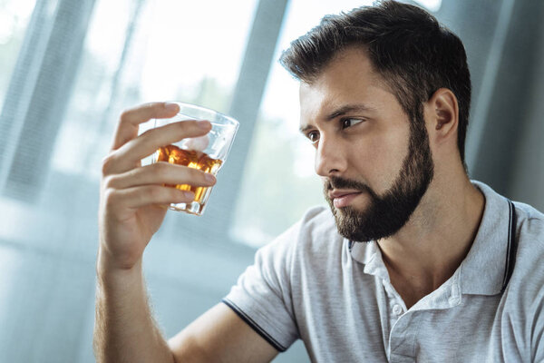 Cheerless addicted man holding a glass with whisky