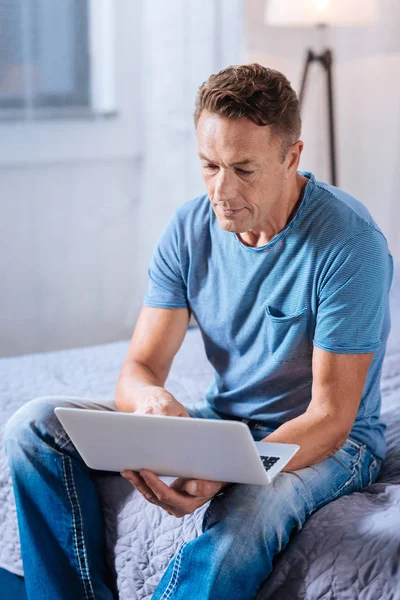 Good-looking man typing on the laptop in bedroom — Stock Photo, Image