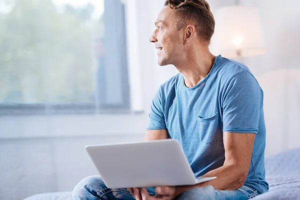 Homem alegre segurando laptop e olhando para a janela — Fotografia de Stock