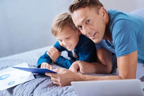 Приятный человек помогает сыну с домашним заданием и улыбается — стоковое фото