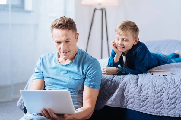 Маленький сын смотрит, как его отец работает на ноутбуке — стоковое фото