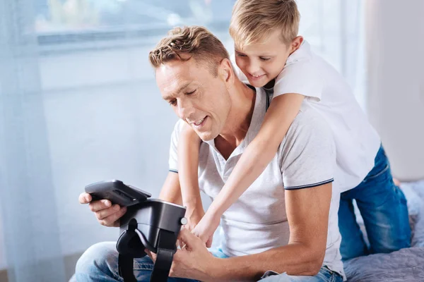 Filho afetuoso abraçando seu pai enquanto ele define fone de ouvido VR — Fotografia de Stock