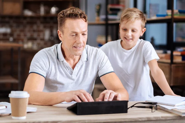 Улыбающийся мальчик смотрит, как отец печатает на планшете — стоковое фото
