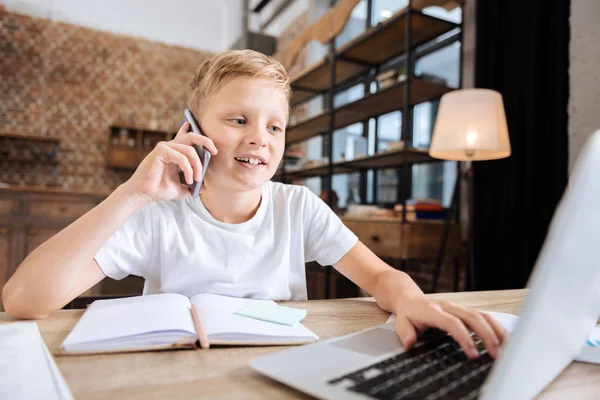 Pre-teen boy talking on the phone while using laptop