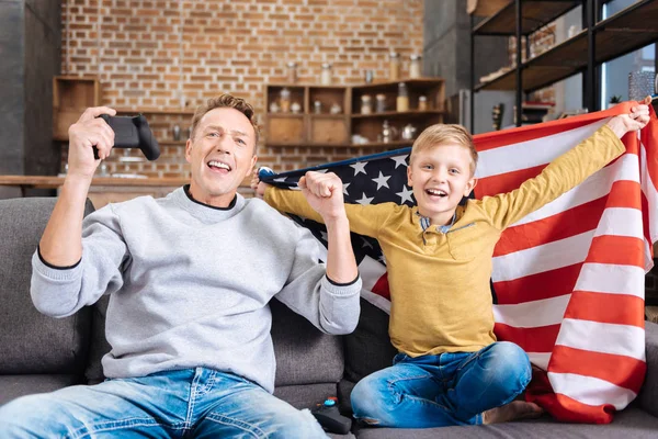 Feliz padre e hijo en la bandera de Estados Unidos celebrando en sofá —  Fotos de Stock