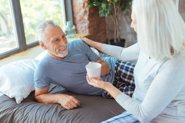 Mujer de edad positiva dando taza de café a su marido amoroso — Foto de Stock