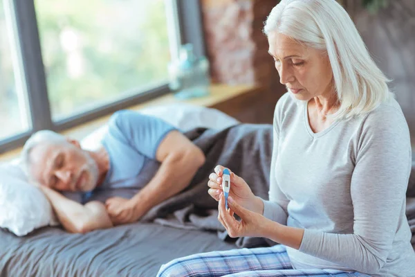 Mujer de edad triste grave sosteniendo un termómetro — Foto de Stock