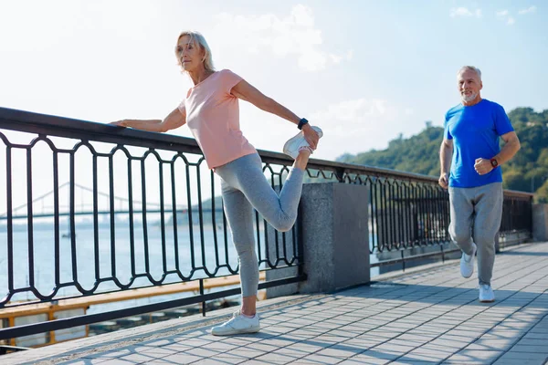 Mujer mayor haciendo ejercicios de estiramiento mientras el hombre trota — Foto de Stock