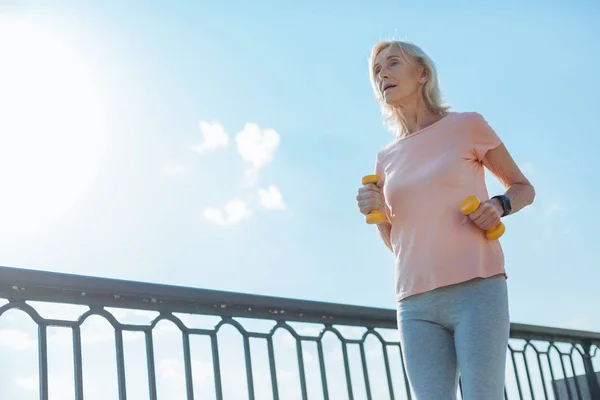 Athletic woman jogging with dumbbells down the bridge — Stock Photo, Image