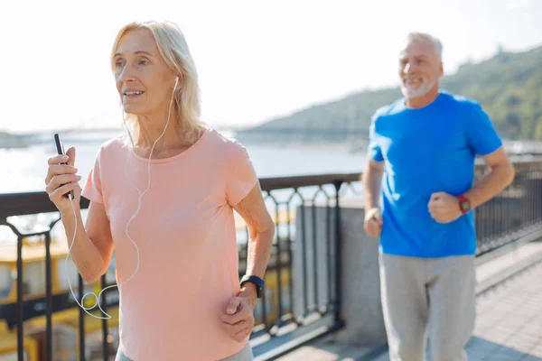 Cheerful senior woman listening to music while jogging — Stock Photo, Image