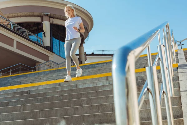 Smal senior kvinna i sportig outfit kör ner för trapporna — Stockfoto